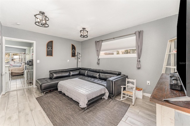 living area with a chandelier, light wood finished floors, baseboards, and a healthy amount of sunlight