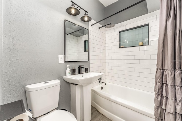 full bathroom with toilet, shower / tub combination, a sink, and a textured wall