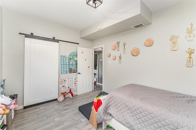 bedroom featuring baseboards, a barn door, visible vents, and light wood-style floors