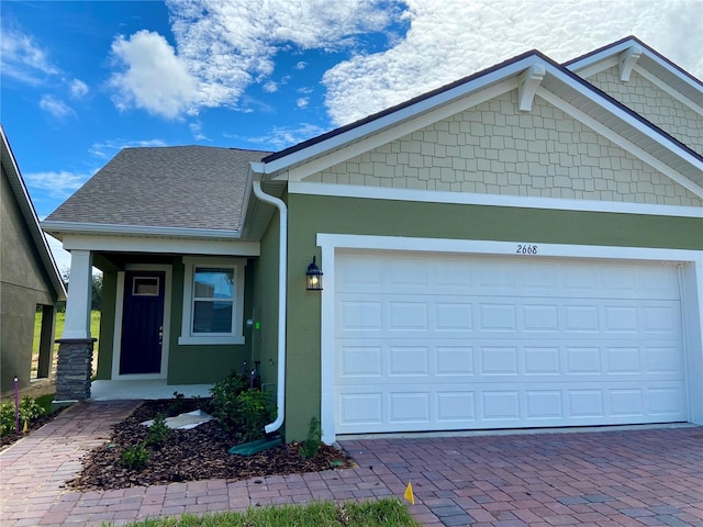 view of front of home with a garage, roof with shingles, decorative driveway, and stucco siding