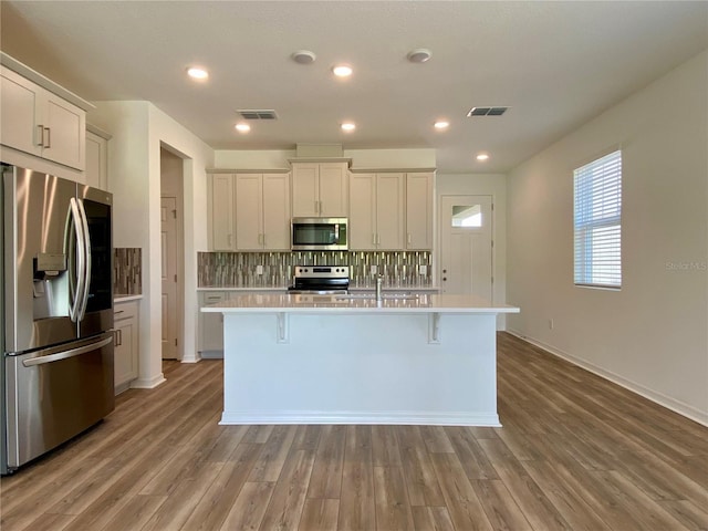 kitchen featuring stainless steel appliances, visible vents, light countertops, backsplash, and a center island with sink