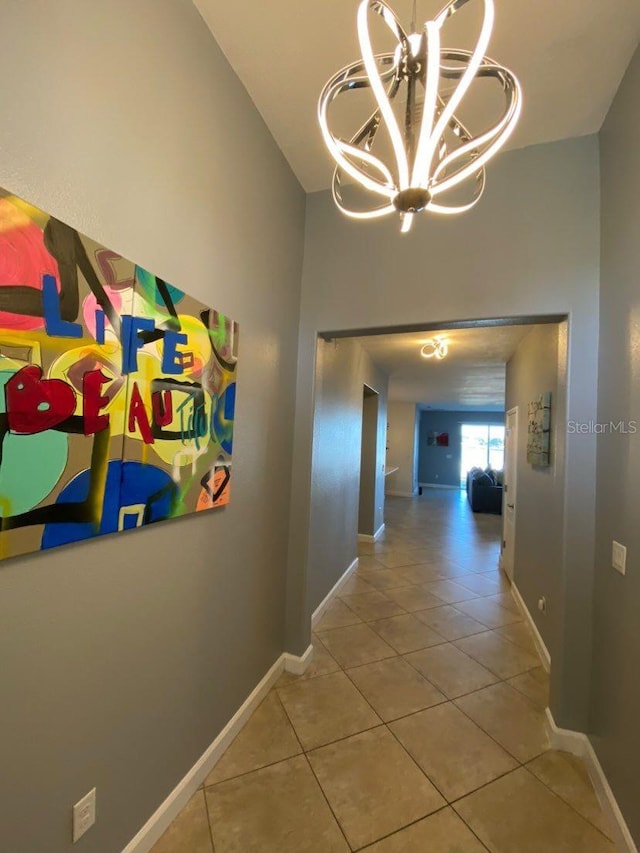 hall featuring tile patterned floors, a chandelier, baseboards, and a towering ceiling