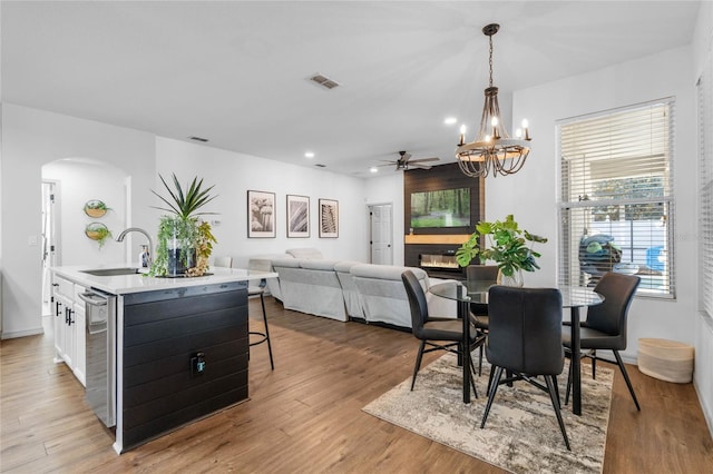 dining space with arched walkways, visible vents, light wood-style flooring, a glass covered fireplace, and ceiling fan with notable chandelier