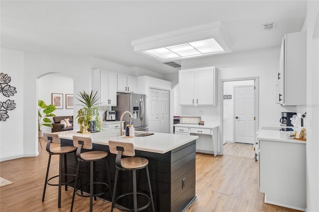 kitchen featuring a breakfast bar, white cabinets, stainless steel fridge, and light wood-style flooring