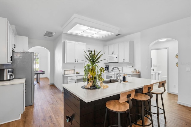 kitchen with arched walkways, light countertops, white microwave, a sink, and a kitchen breakfast bar