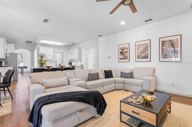 living room featuring arched walkways, visible vents, and light wood-style flooring