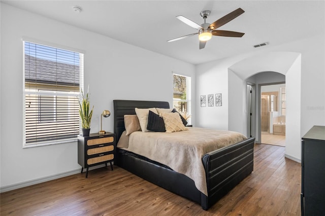 bedroom featuring arched walkways, wood finished floors, visible vents, and baseboards