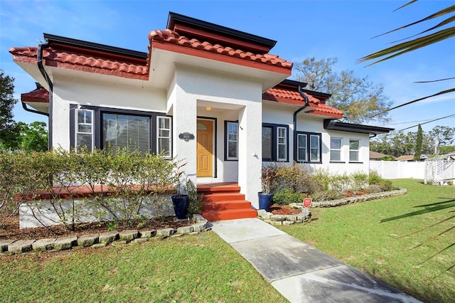 mediterranean / spanish-style house featuring fence, a tiled roof, a front lawn, and stucco siding