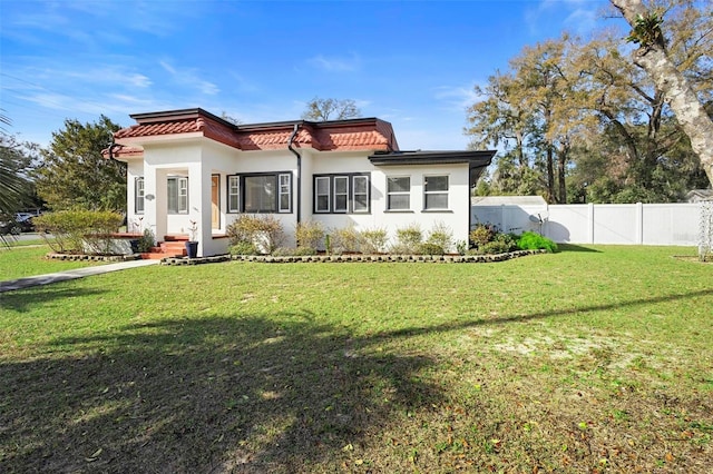 rear view of house with stucco siding, a tile roof, fence, and a yard