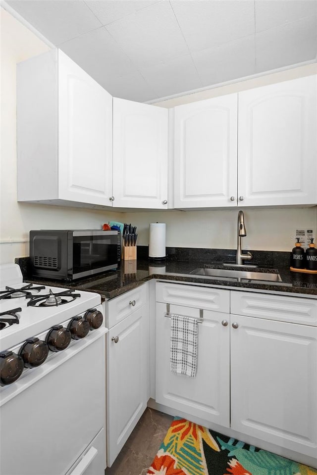 kitchen featuring dark stone counters, a sink, range, and white cabinetry