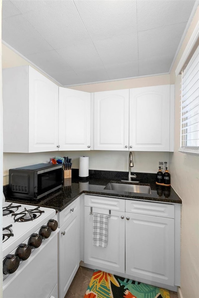 kitchen with black microwave, dark stone countertops, a sink, and white cabinetry