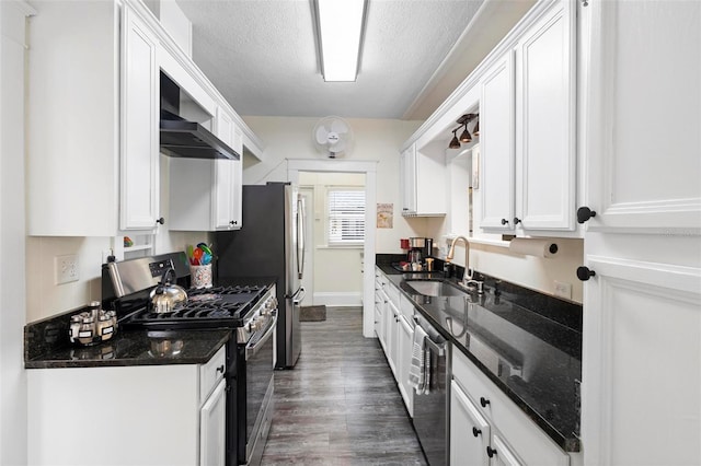 kitchen featuring wall chimney range hood, appliances with stainless steel finishes, a sink, and white cabinets