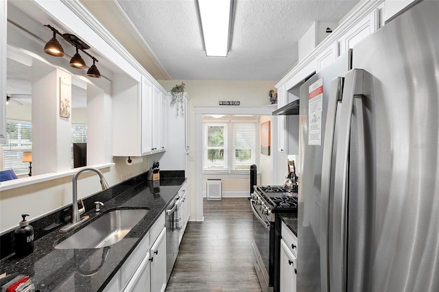 kitchen with appliances with stainless steel finishes, dark wood-type flooring, a textured ceiling, white cabinetry, and a sink