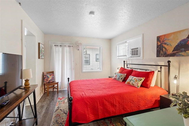 bedroom with a wall unit AC, a textured ceiling, and wood finished floors