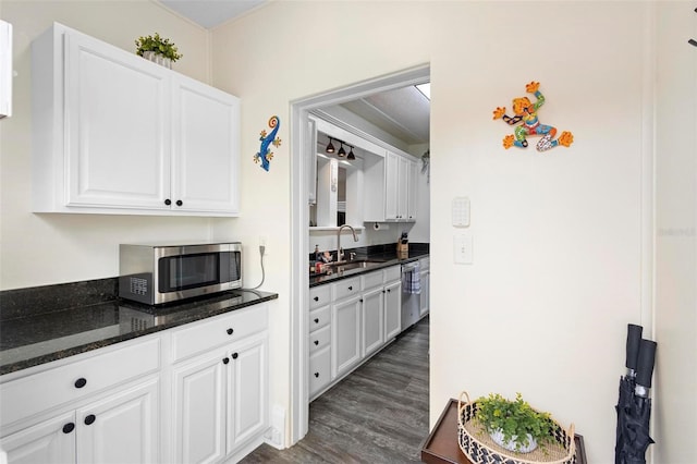 kitchen featuring white cabinets, appliances with stainless steel finishes, dark wood-type flooring, dark stone countertops, and a sink