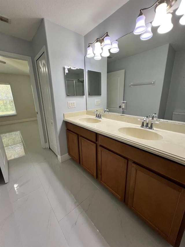 bathroom featuring marble finish floor, a sink, baseboards, and double vanity