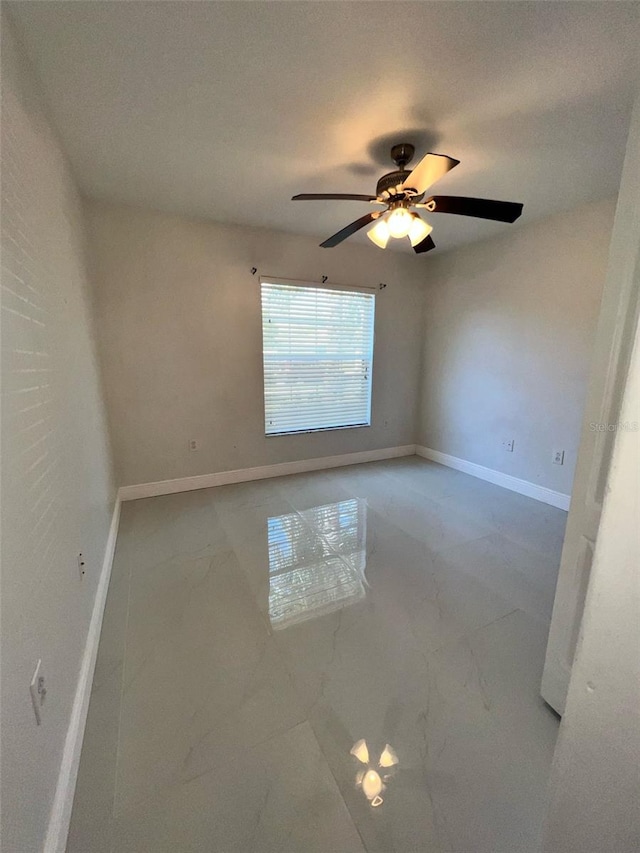 spare room with marble finish floor, baseboards, and a ceiling fan