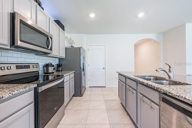 kitchen with stainless steel appliances, decorative backsplash, light tile patterned flooring, a sink, and light stone countertops