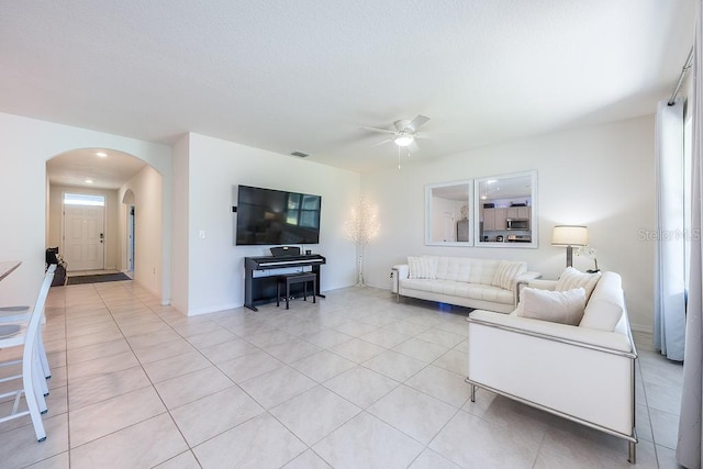 living area with light tile patterned floors, visible vents, arched walkways, baseboards, and a ceiling fan