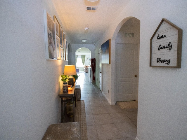 hall with arched walkways, visible vents, and light tile patterned floors