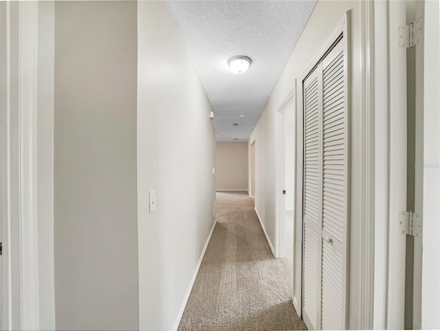 hall with a textured ceiling, carpet flooring, and baseboards