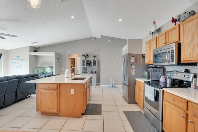 kitchen with light tile patterned floors, appliances with stainless steel finishes, open floor plan, vaulted ceiling, and a sink