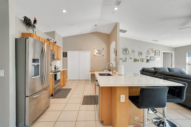 kitchen with lofted ceiling, light tile patterned flooring, a sink, open floor plan, and appliances with stainless steel finishes