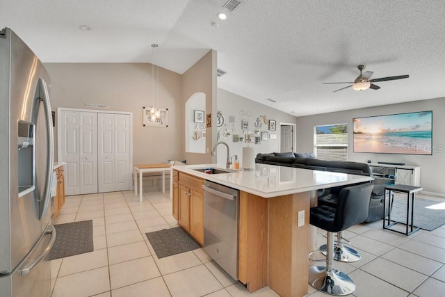 kitchen featuring light tile patterned floors, stainless steel appliances, a sink, vaulted ceiling, and a center island with sink