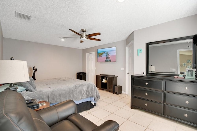 bedroom with a textured ceiling, light tile patterned flooring, visible vents, a ceiling fan, and a closet