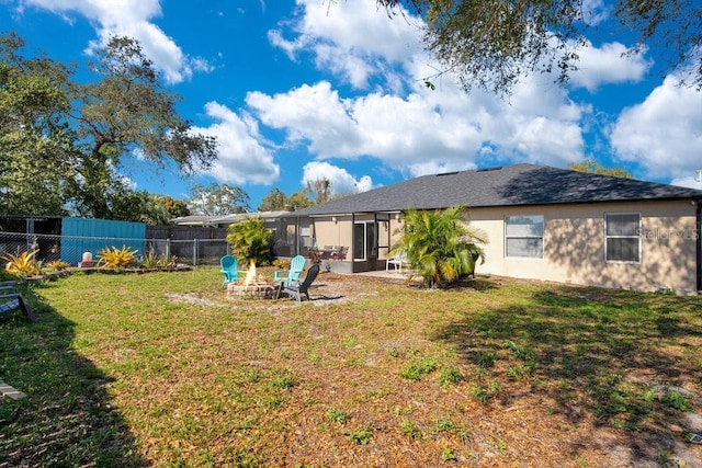 rear view of house featuring a fire pit, a lawn, fence, and a sunroom