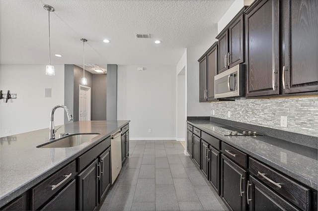 kitchen featuring black electric stovetop, stainless steel microwave, visible vents, decorative backsplash, and a sink