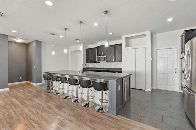 kitchen with decorative backsplash, a kitchen island with sink, stainless steel appliances, a kitchen bar, and a sink