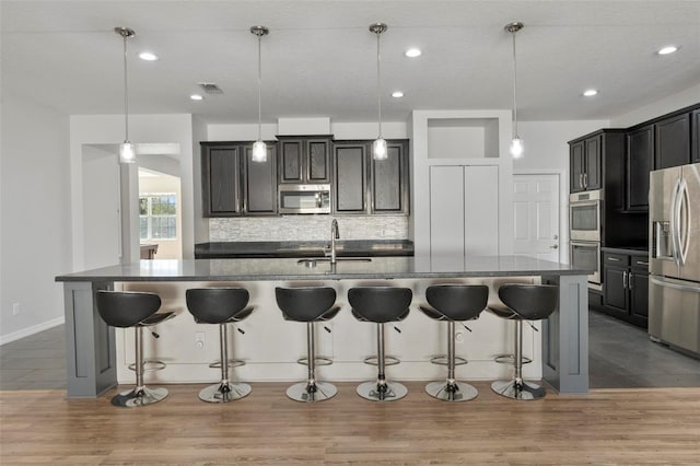 kitchen with wood finished floors, appliances with stainless steel finishes, a sink, and tasteful backsplash