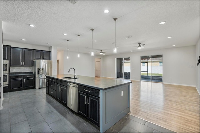 kitchen with a center island with sink, appliances with stainless steel finishes, open floor plan, decorative light fixtures, and a sink