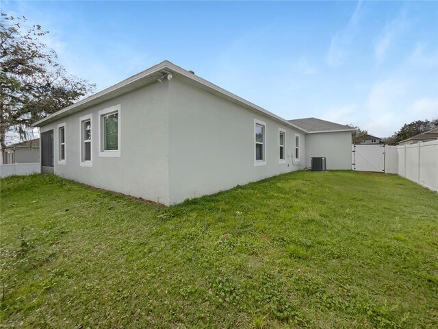15120 Zenith Ave, Mascotte, FL 34753 - back of property featuring a fenced backyard, central air condition unit, a lawn, a gate, and stucco siding