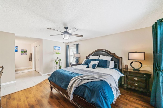 bedroom with a closet, ceiling fan, a textured ceiling, wood finished floors, and baseboards