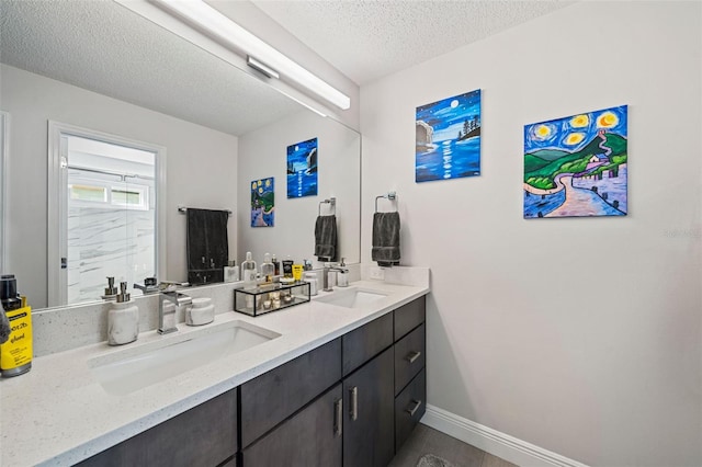 bathroom with a textured ceiling, double vanity, a sink, and baseboards