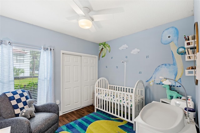 bedroom featuring a ceiling fan, a nursery area, a closet, and wood finished floors