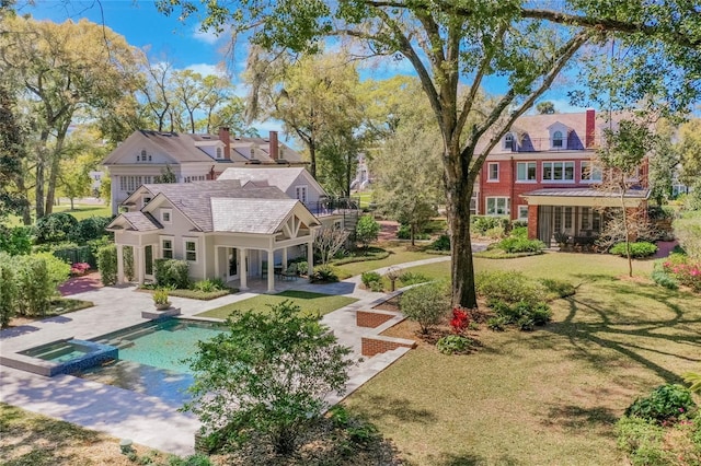 rear view of house featuring a pool with connected hot tub, a lawn, and a patio