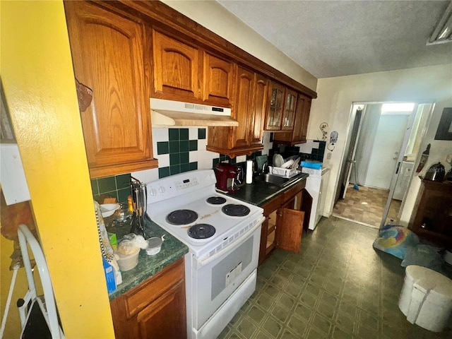 kitchen with dark floors, white electric stove, backsplash, brown cabinetry, and under cabinet range hood