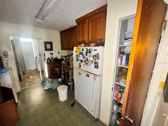 kitchen featuring brown cabinetry, freestanding refrigerator, a textured ceiling, and dark floors