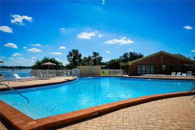 pool featuring a patio area, fence, and a water view