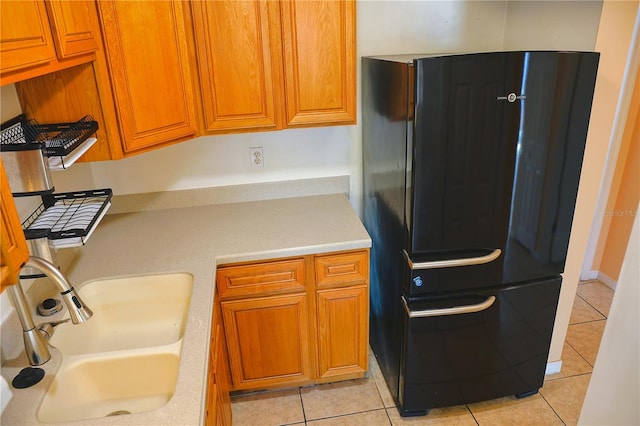 kitchen featuring brown cabinets, light tile patterned floors, light countertops, freestanding refrigerator, and a sink