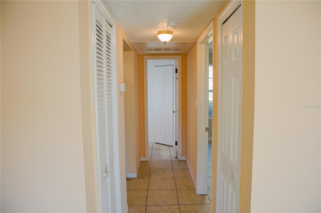 hallway with a textured ceiling, light tile patterned floors, visible vents, and baseboards