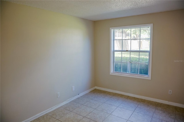 empty room with light tile patterned floors, baseboards, and a textured ceiling