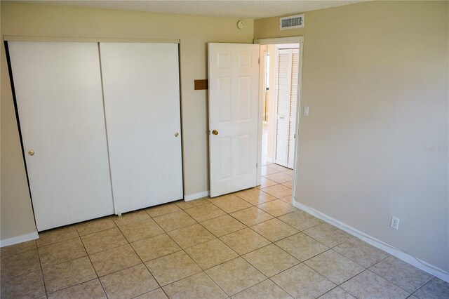 unfurnished bedroom with light tile patterned floors, a textured ceiling, visible vents, baseboards, and a closet