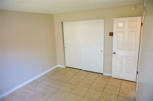 unfurnished bedroom with light tile patterned floors, a closet, a textured ceiling, and baseboards