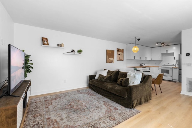 living room with light wood-style flooring, rail lighting, baseboards, and visible vents