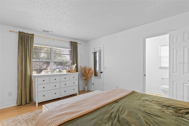 bedroom with baseboards, visible vents, ensuite bath, light wood-style floors, and a textured ceiling