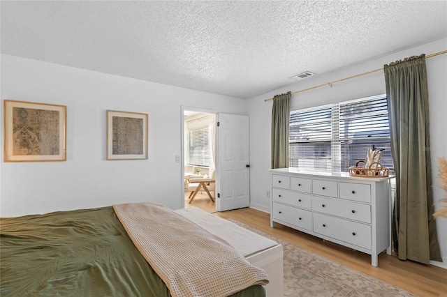 bedroom featuring a textured ceiling, ensuite bath, visible vents, and light wood-type flooring